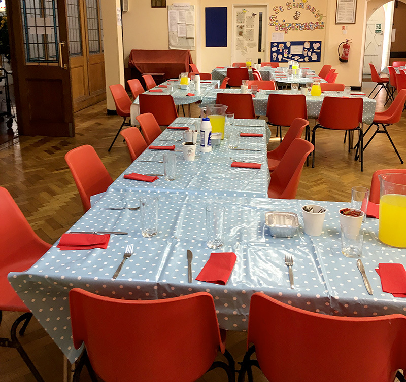 Tables, chairs and place settings set out for Sunday Suppers in St Simon’s lower hall.